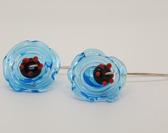 May include: A pair of blue glass earrings with a black and red center. The earrings are shaped like a flower with a swirl design.