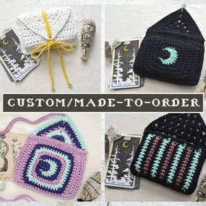 May include: Four crocheted bags with a crescent moon design. The bags are in different colours, including white, black, purple, and pink. The bags are made to order and are perfect for holding tarot cards or other small items. CUSTOM/MADE-TO-ORDER