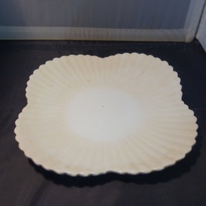 May include: A white ceramic plate with a scalloped edge and a fluted design. The plate is slightly curved and has a smooth, glossy finish.