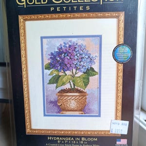 Può includere: Un kit per punto croce contato Dimensions The Gold Collection Petites intitolato Hydrangea in Bloom. La confezione mostra un disegno finito di fiori di ortensia viola e blu in un vaso marrone, che misura 13 cm per 18 cm.