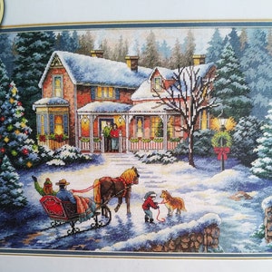 Puede incluir: Un kit de bordado de punto de cruz con una escena invernal que muestra una casa de ladrillo cubierta de nieve, un árbol de Navidad decorado y un trineo tirado por un caballo. Dos figuras van en el trineo y un niño pasea a un perro en la nieve.