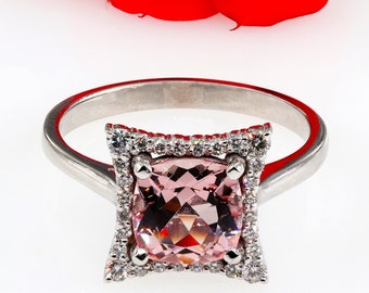 Könnte beinhalten: Ein silberner Ring mit einem quadratischen rosafarbenen Edelstein, der von einem Heiligenschein aus kleineren Diamanten umgeben ist.