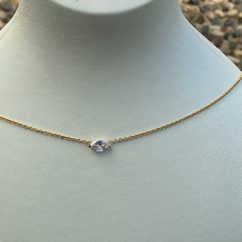 May include: A delicate gold chain necklace with a single marquise-shaped clear gemstone pendant.