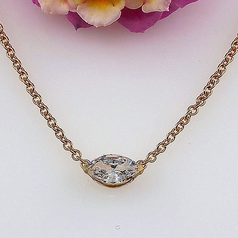 May include: A gold chain necklace with a single, clear, marquise-shaped gemstone pendant.