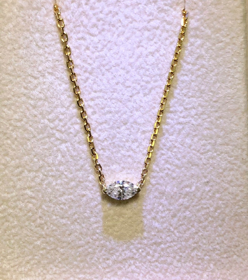 May include: A delicate gold chain necklace with a single, clear, oval-shaped diamond pendant.