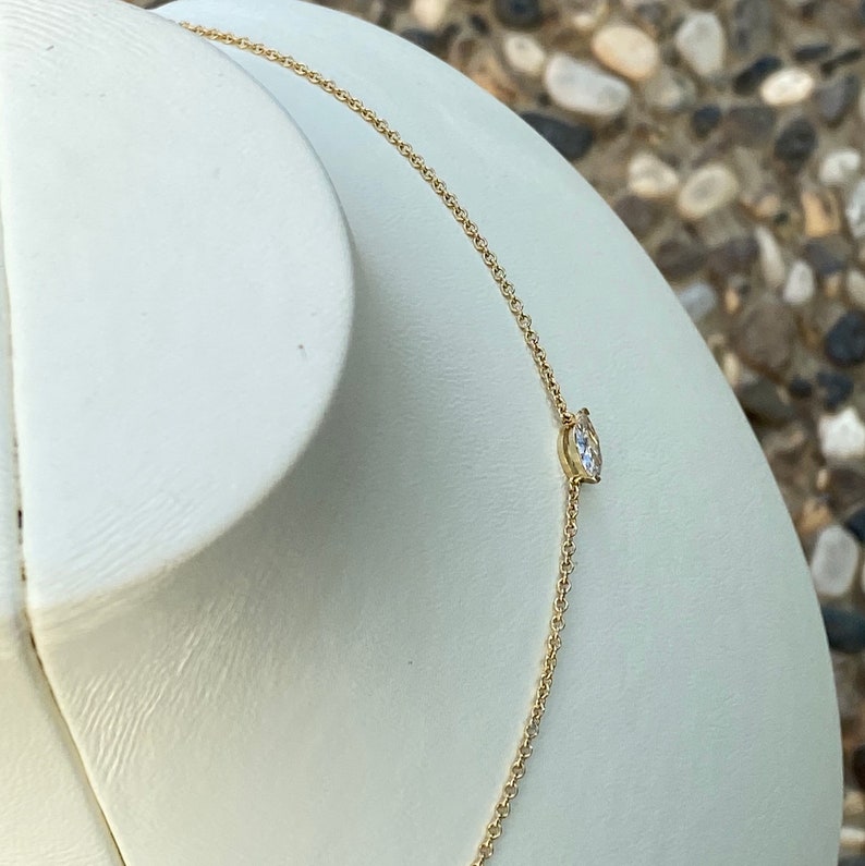 May include: A delicate gold chain necklace with a single, clear, round gemstone pendant.