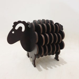 May include: A black wooden sheep-shaped coaster with a white ear. The coaster is made of multiple layers of wood, creating a 3D effect.