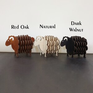 May include: Three wooden sheep coasters in different wood stains: red oak, natural, and dark walnut. The coasters are shaped like sheep with a curly tail and a small head.