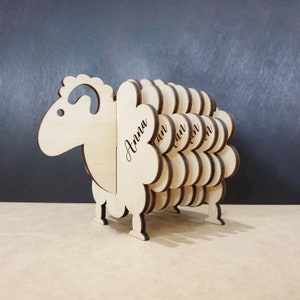 May include: A wooden sheep-shaped coaster set with the names "Anna", "Ian", "Ryan", "Ron", and "Jon" engraved on the sides.