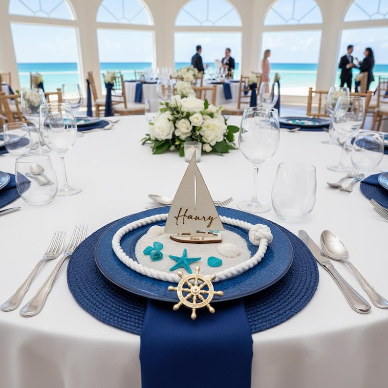 Puede incluir: Decoraci&oacute;n de mesa de tem&aacute;tica n&aacute;utica con mantel blanco, platos azules y un velero decorativo. El conjunto incluye un tim&oacute;n dorado, estrellas de mar y un adorno de cuerda. El nombre "Harry" est&aacute; escrito en el velero.
