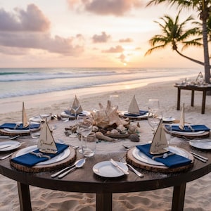 Puede incluir: Una mesa redonda de madera preparada para un evento en la playa. Cada cubierto incluye un plato blanco, una servilleta azul, cubiertos y una tarjeta de lugar con forma de velero de madera. La mesa est&aacute; decorada con conchas marinas y madera flotante, con una puesta de sol al fondo.