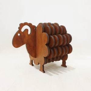 May include: A wooden sheep coaster with a brown finish. The sheep is made of multiple layers of wood, creating a 3D effect.