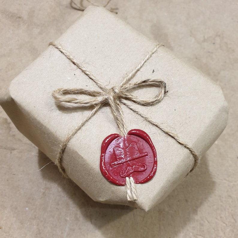 May include: A brown paper parcel tied with twine and sealed with a red wax stamp. The stamp has a design of a hat and a moustache.