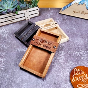 May include: Three wooden trays with different designs. The first tray is black and says "Paperlu" on it. The second tray is brown and says "Steak House" on it. The third tray is light brown and says "Restaurant" on it.