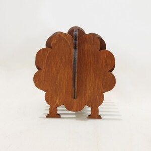 May include: A wooden turkey napkin holder with a brown stain finish. The turkey has a rounded body and a long neck. It has four legs and a tail.