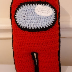 Puede incluir: Juguete de peluche rojo tejido a crochet con forma del personaje del videojuego Among Us. El juguete tiene un contorno negro y una visera azul y blanca.