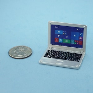 May include: A silver laptop computer with a black keyboard and a screen displaying the Windows Start menu.