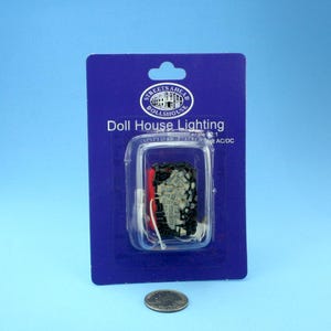 May include: A dollhouse lighting kit in a clear plastic package on a blue card. The card has the text "Doll House Lighting" and a logo. A coin is in front of the package.