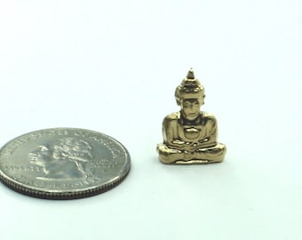 以下が含まれることがあります： 座った姿勢の小さな金色の仏像。大きさ比較のためにコインの隣に配置されています。仏像は詳細な顔と尖った頭飾りをしています。背景は白です。コインは米国の25セント硬貨です。