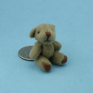 May include: A small, light brown teddy bear with brown felt paws and a brown nose. The bear is sitting on a light blue surface.