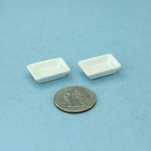 May include: Two small white rectangular ceramic dishes on a light blue background. A silver US quarter is in the center of the image for scale.