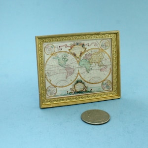 May include: A miniature framed world map with a gold-colored ornate frame. The map features detailed illustrations of continents and oceans in various colors. A quarter coin is next to the frame for size comparison. The map is set against a light blue background.