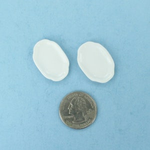 May include: Two white ceramic oval-shaped plates, approximately the size of a US quarter.