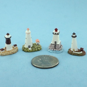 May include: Four miniature lighthouse figurines, each with a white tower and a different colored roof, are displayed on a light blue surface. A US quarter is included for scale.