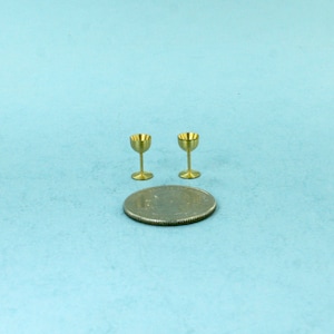 May include: Two small gold-colored metal goblets on a blue background with a silver coin for scale.