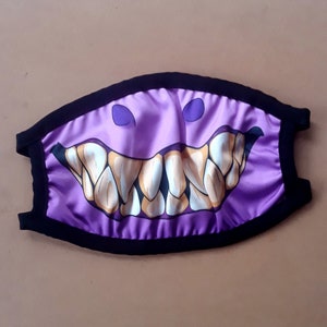 Puede incluir: Máscara facial morada con borde negro y un gráfico de una gran sonrisa de dientes.