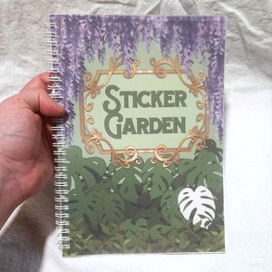 May include: A green and gold sticker garden journal with a spiral binding. The cover features a decorative gold frame with the words "Sticker Garden" in a stylised font. The background is a green and purple floral pattern.