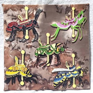 May include: A collection of five insect-themed enamel pins. The pins feature a red ant, a green grasshopper, a black beetle, a yellow bee, and a blue and yellow bee, all designed with carousel-style poles and decorative elements. The pins are set against a mottled brown background.