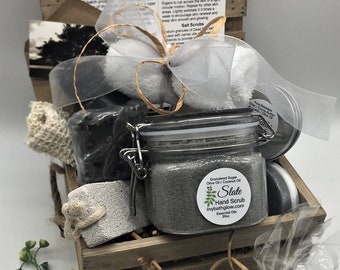 May include: A wooden crate filled with bath products, including a jar of hand scrub, a cologne balm tin, and wrapped soaps. The crate is tied with a ribbon and includes a card with product information.
