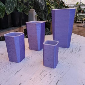 Könnte beinhalten: Ein Set aus vier violetten Pflanzgefäßen mit einer texturierten, hexagonalen Außenseite und einer glatten, hellen Innenseite. Die Gefäße variieren in Höhe und Breite und haben ein konisches Design, das sich zur Basis hin verjüngt.