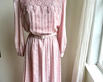 May include: A pink vintage dress with a white lace collar and a pleated skirt. The dress has a belt and long sleeves.