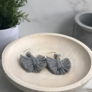 May include: A pair of gray tassel earrings with a knotted design. The earrings are displayed on a light gray bowl.
