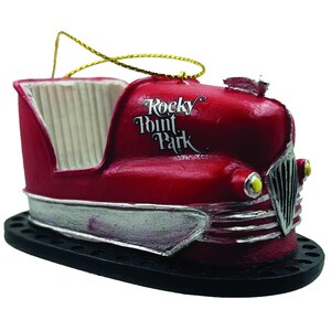May include: A red bumper car ornament with silver trim and the words "Rocky Point Park". The ornament has a gold hanging string and sits on a black base. The bumper car design is vintage.