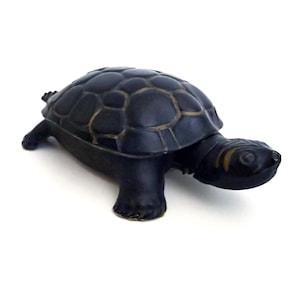 May include: A small, dark-colored turtle figurine with a matte black finish. The shell features a raised, segmented pattern with subtle brown highlights along the edges of the plates. The head has a smooth texture with faint yellow markings.