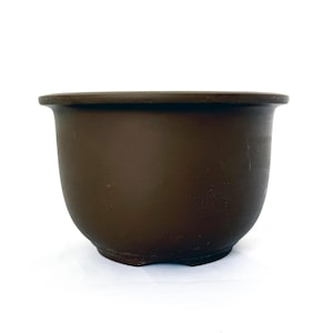 May include: A dark brown, matte-finished ceramic bowl with a wide, flared rim and a rounded, deep basin. The vessel features a smooth, uniform surface texture and a sturdy, slightly elevated base, presenting a simple, functional design.