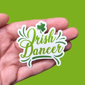 May include: A white sticker with green lettering that reads "Irish Dancer". A green shamrock is above the text.