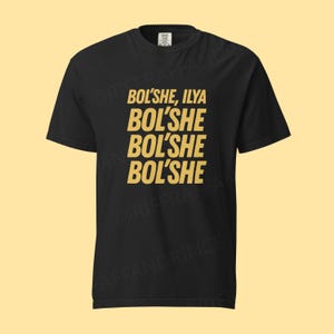 May include: Black t-shirt featuring the gold text "BOL'SHE, ILYA" stacked on top of three repetitions of "BOL'SHE". The shirt has a crew neck and short sleeves, a classic casual design.