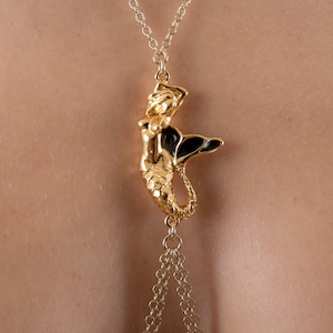 May include: A gold chain body jewelry piece with a mermaid pendant. The mermaid is gold with black enamel details.