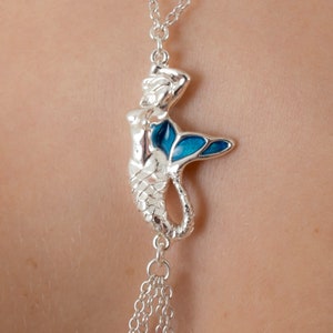 May include: Silver chain necklace with a mermaid pendant. The mermaid is silver with blue enamel on her tail.