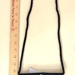 May include: A black fabric bag with a black braided strap. The bag has a white plastic hook attached to the top.