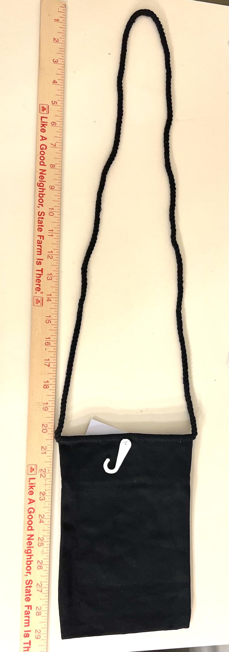 May include: A black fabric bag with a black braided strap. The bag has a white plastic hook attached to the top.
