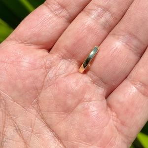 May include: A simple gold band ring, shown on a hand.