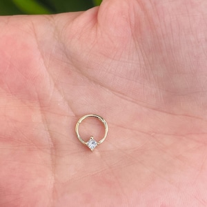 Pode incluir: Um brinco de argola de ouro com uma pequena gema quadrada transparente.