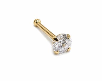 May include: A gold nose stud featuring a clear, round-cut cubic zirconia gemstone. The stud has a straight post and a small ball on the opposite end of the gemstone. The jewelry is set against a white background.