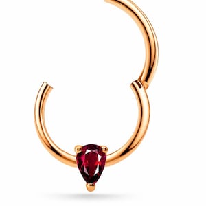 May include: A rose gold hinged segment ring featuring a single pear-shaped deep red gemstone set at the base. The circular hoop has a smooth polished finish and a secure clicker mechanism, designed for body piercings with a minimalist aesthetic.
