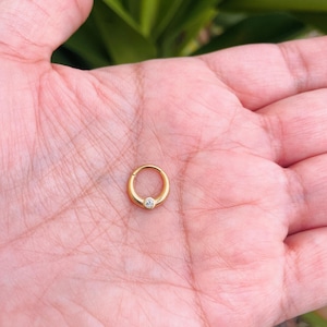 May include: A gold hoop earring with a small clear gemstone set in the center.